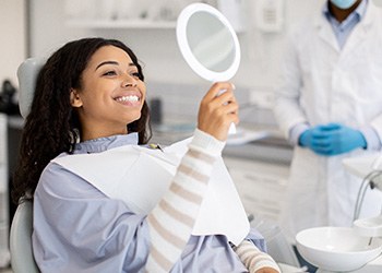 Woman smiling at reflection in handheld mirror