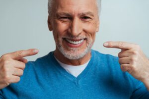 Older man with dentures pointing at smile.