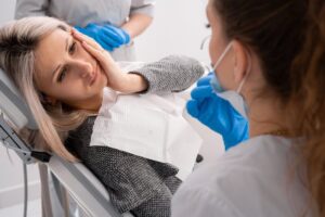 Woman in dentist's chair holding jaw in pain.