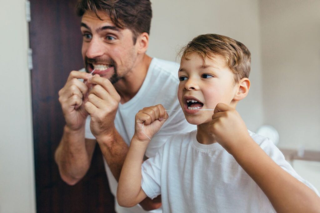 A father and son flossing their teeth in a mirror