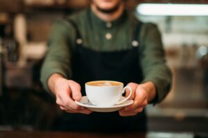 Man in green shirt holding out cup of coffee